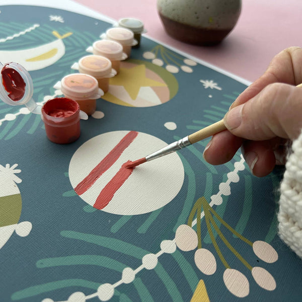 Person painting a design on a decorative mat with a brush and red paint.