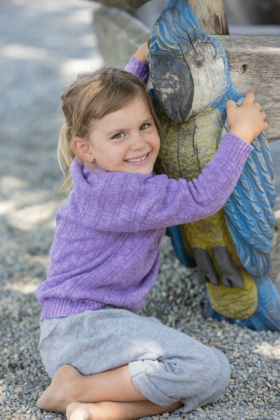 A child sitting on the ground by a boat wearing grey knitted linen trousers with a soft elastic waistband and rolled-up legs, with knitted back pockets.