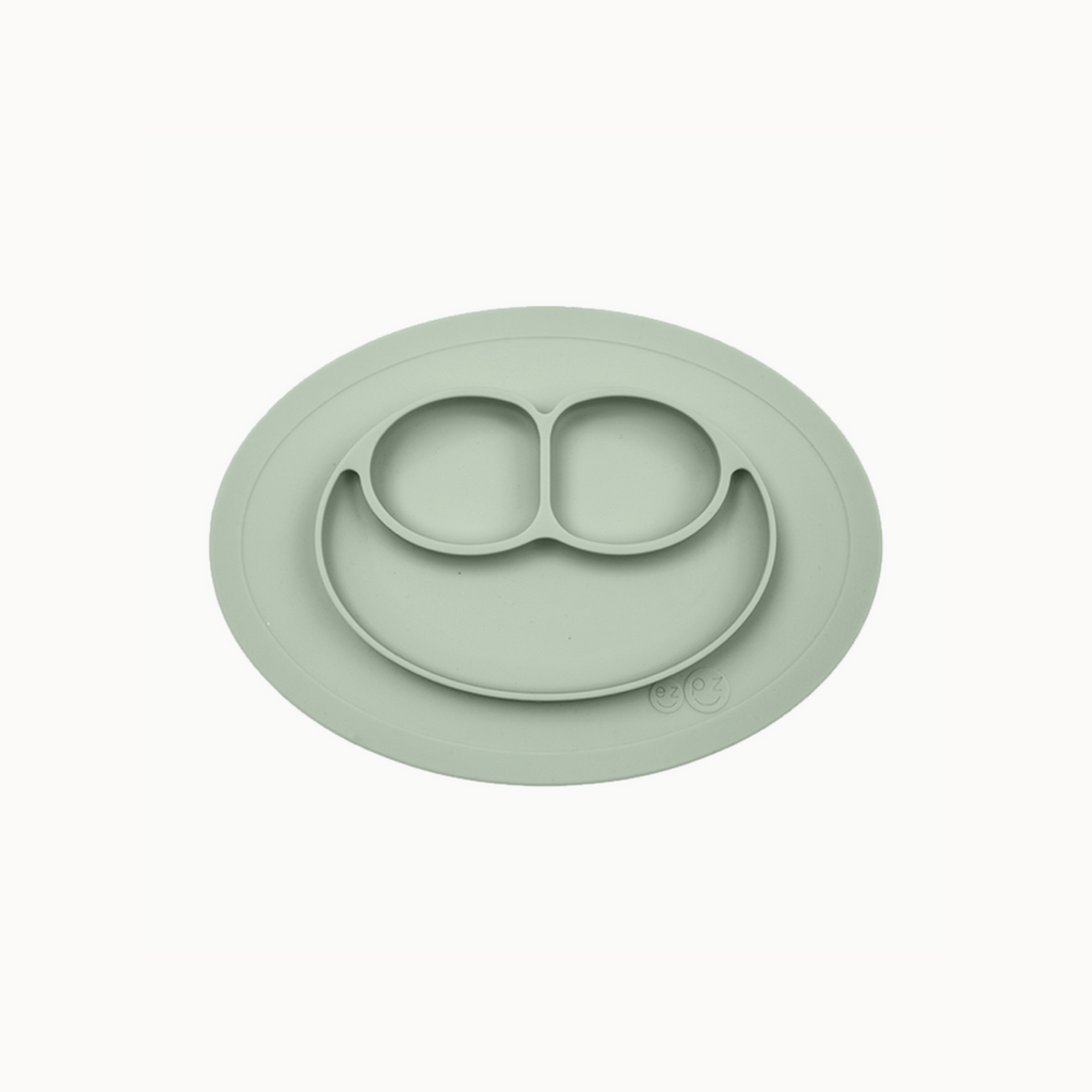 A green ezpz Mini Mat, an all-in-one placemat and plate designed for mealtime, suctioning to a table surface.