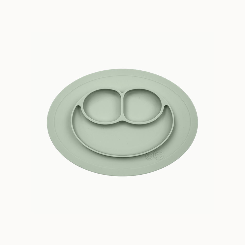 A green ezpz Mini Mat, an all-in-one placemat and plate designed for mealtime, suctioning to a table surface.