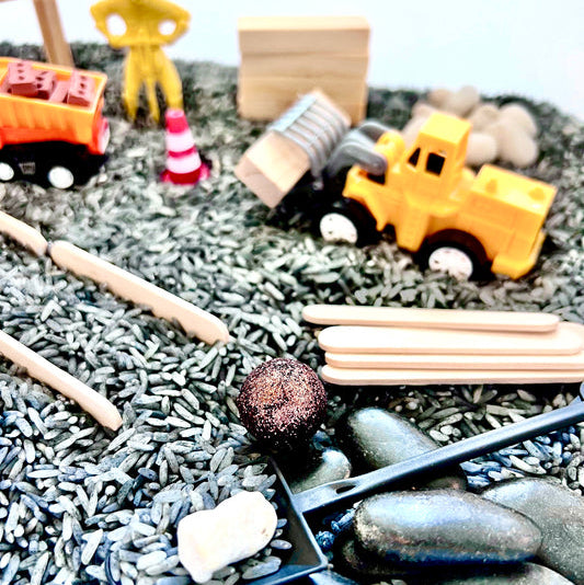 Toy construction set with mini figures, trucks, and tools on a textured surface.