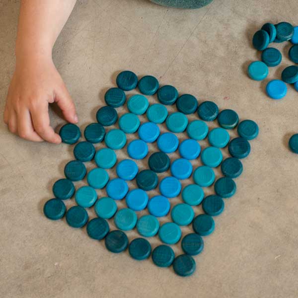 Blue circular tiles arranged on a beige floor with a child's hand reaching towards them.