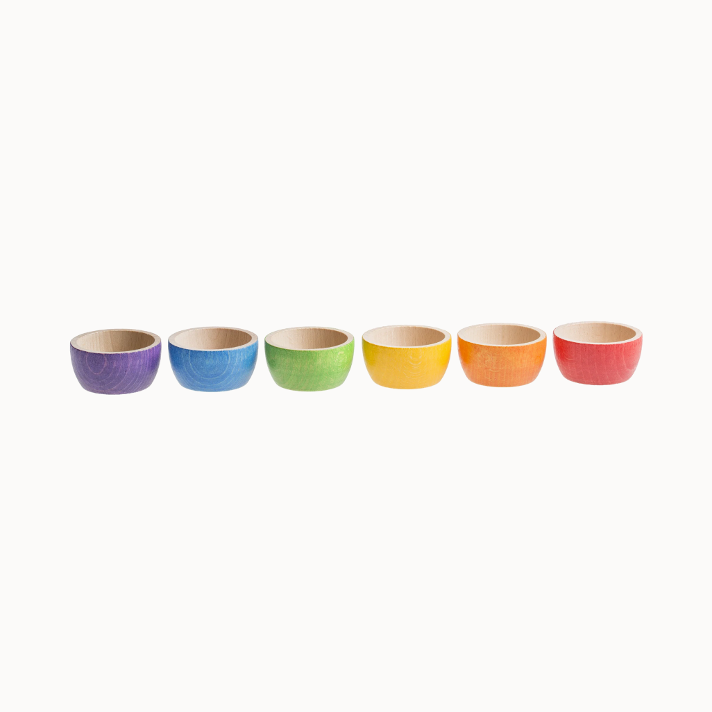 A set of six wooden bowls in a rainbow color palette, displayed in a row.
