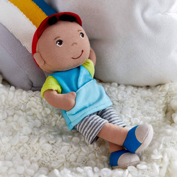 Plush toy of a child wearing a blue shirt, striped shorts, and a red cap on a white surface.