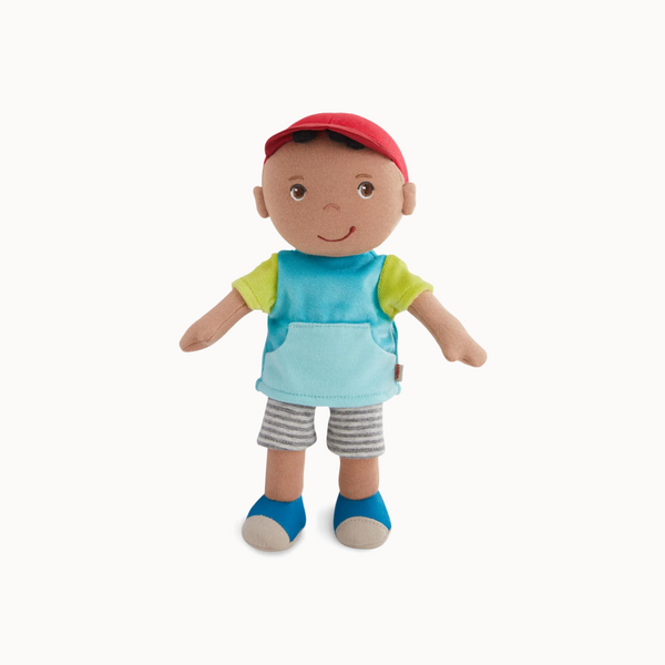 Plush toy doll with a red cap, blue shirt, green sleeves, gray shorts, and blue socks on a white background