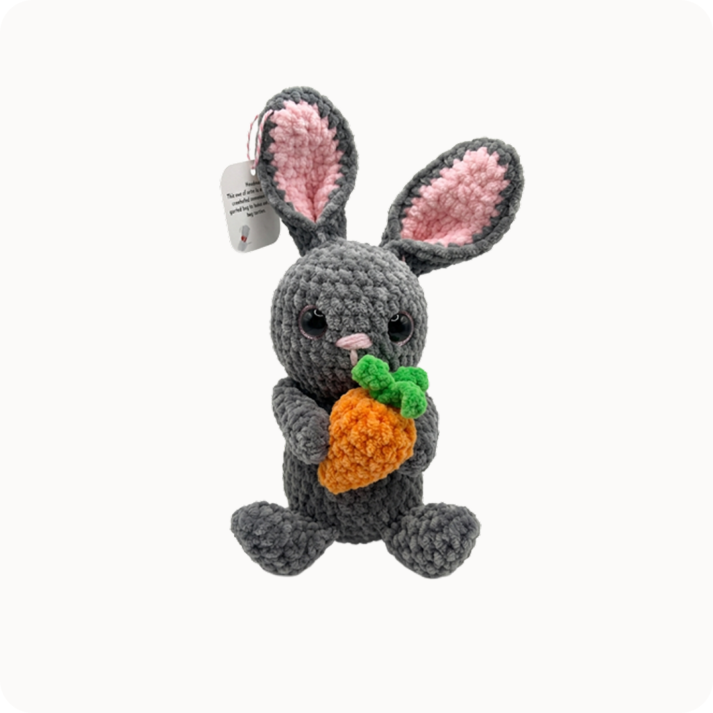 Gray plush bunny toy resembling a rabbit with pink ears and a carrot on a white background
