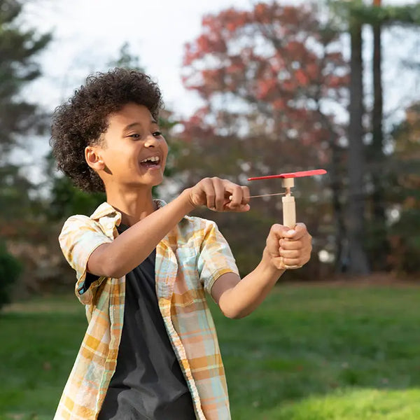 Packaged Huckleberry Pull Helicopter toy designed by Koens & Middlekoop, made from wood and polyester string, with a red launcher, Being pulled by boy