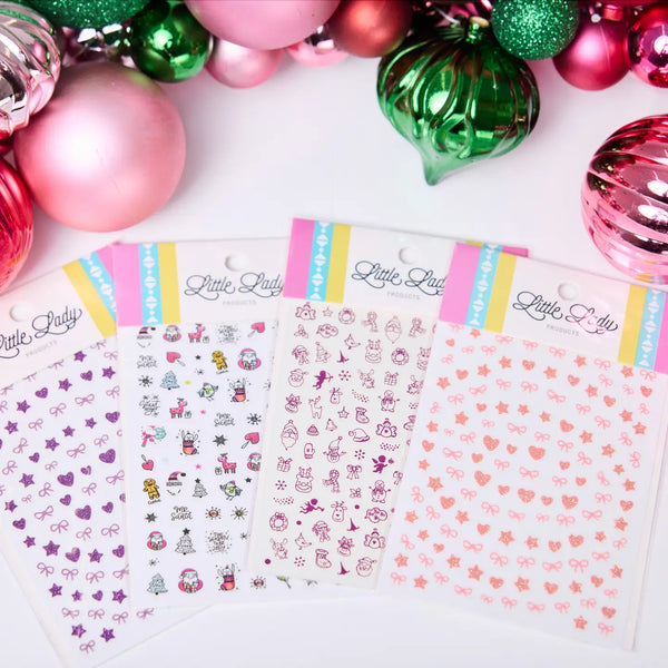 Sticker sheets with decorative designs on a white surface surrounded by colorful Christmas ornaments.