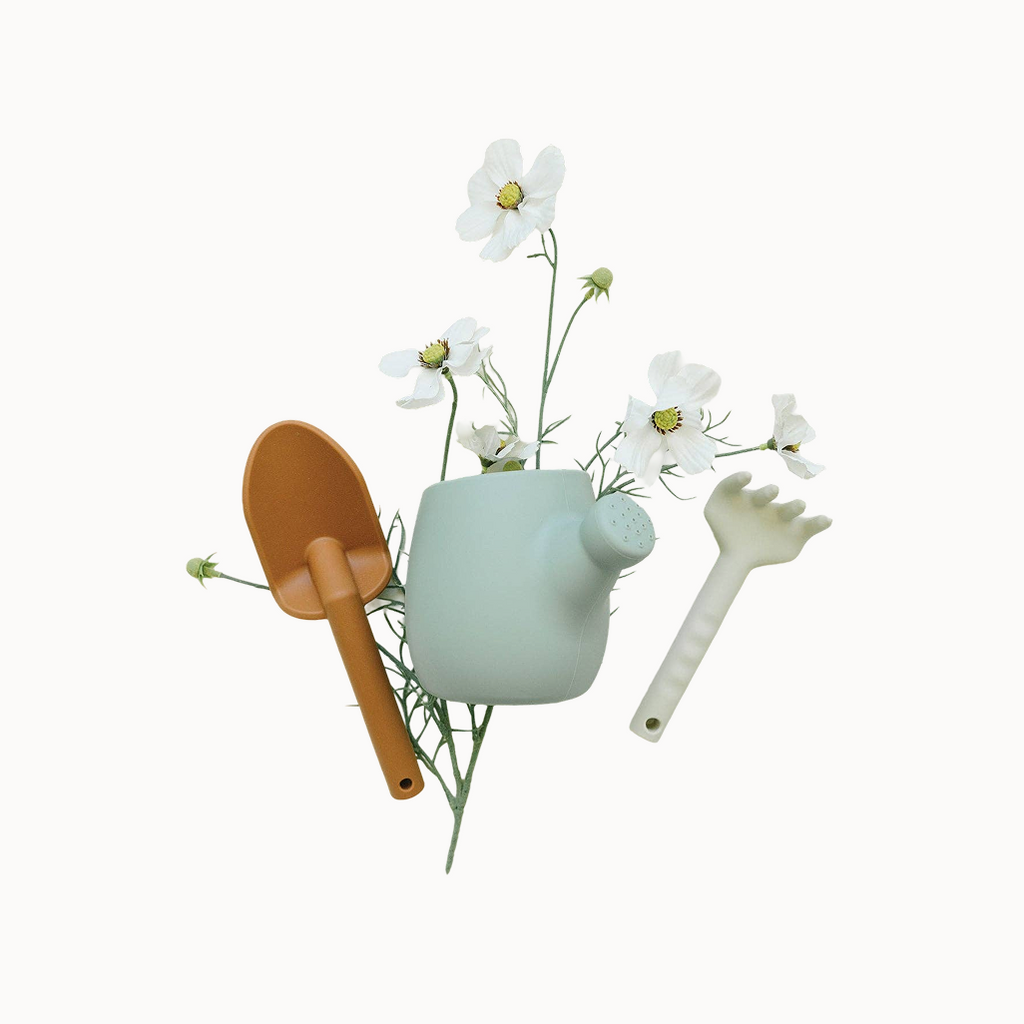 Decorative set with a small green teapot, brown shovel, and white flowers on a light background