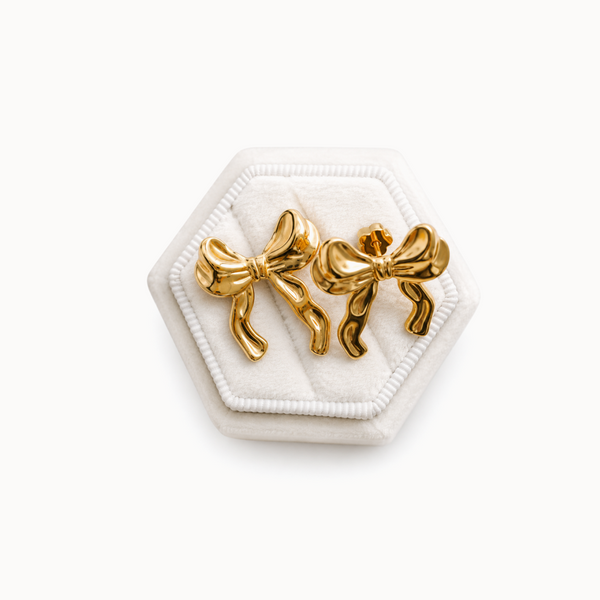 Gold bow-shaped earrings on a white hexagonal stand with a white background