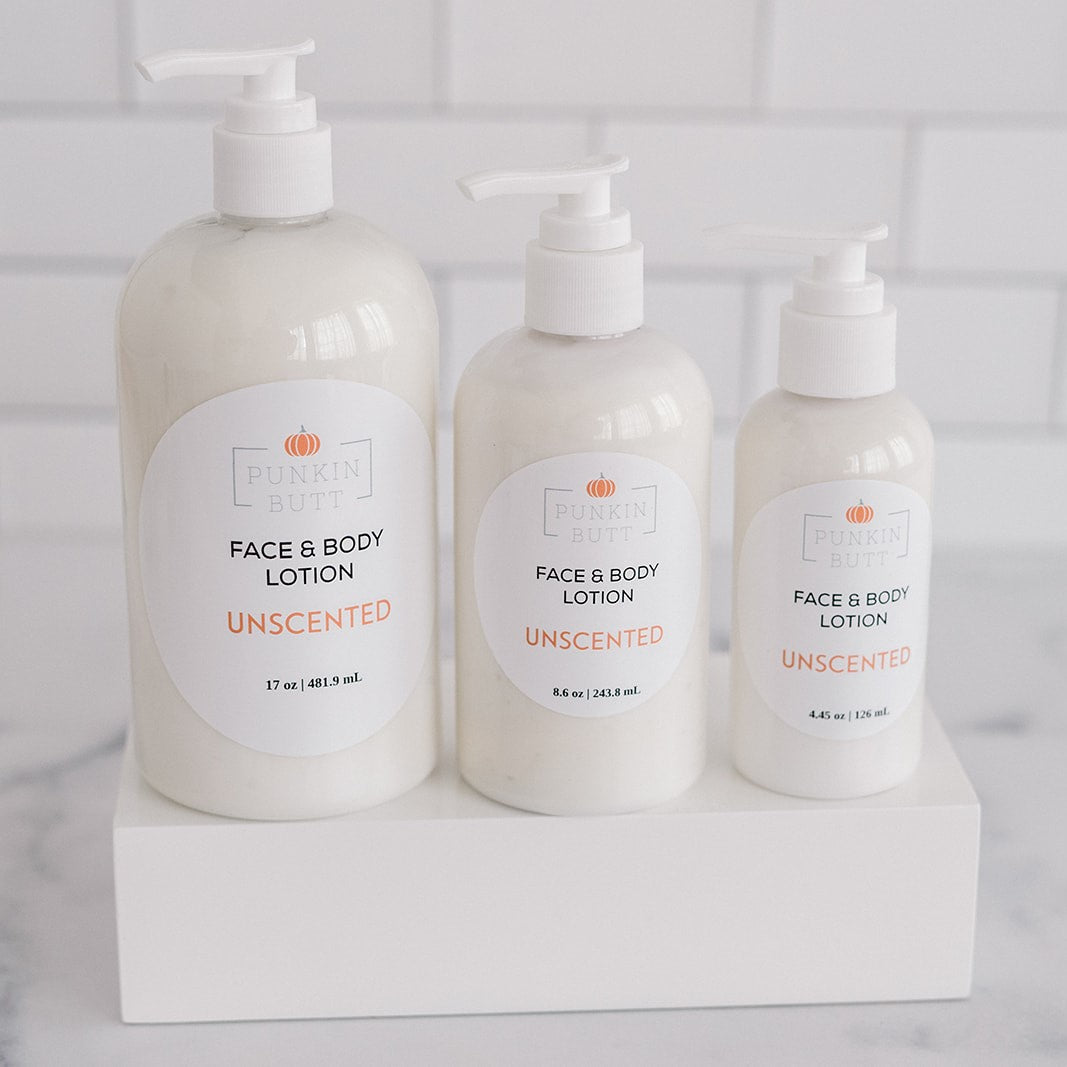 Three bottles of unscented face and body lotion on a white surface with a light gray tiled background.