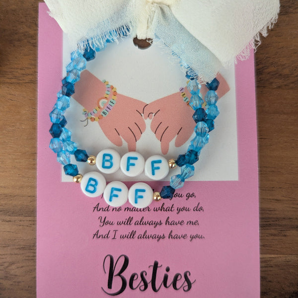 Two blue beaded bracelets with 'BFF' letters on a pink card with text, against a wooden background.