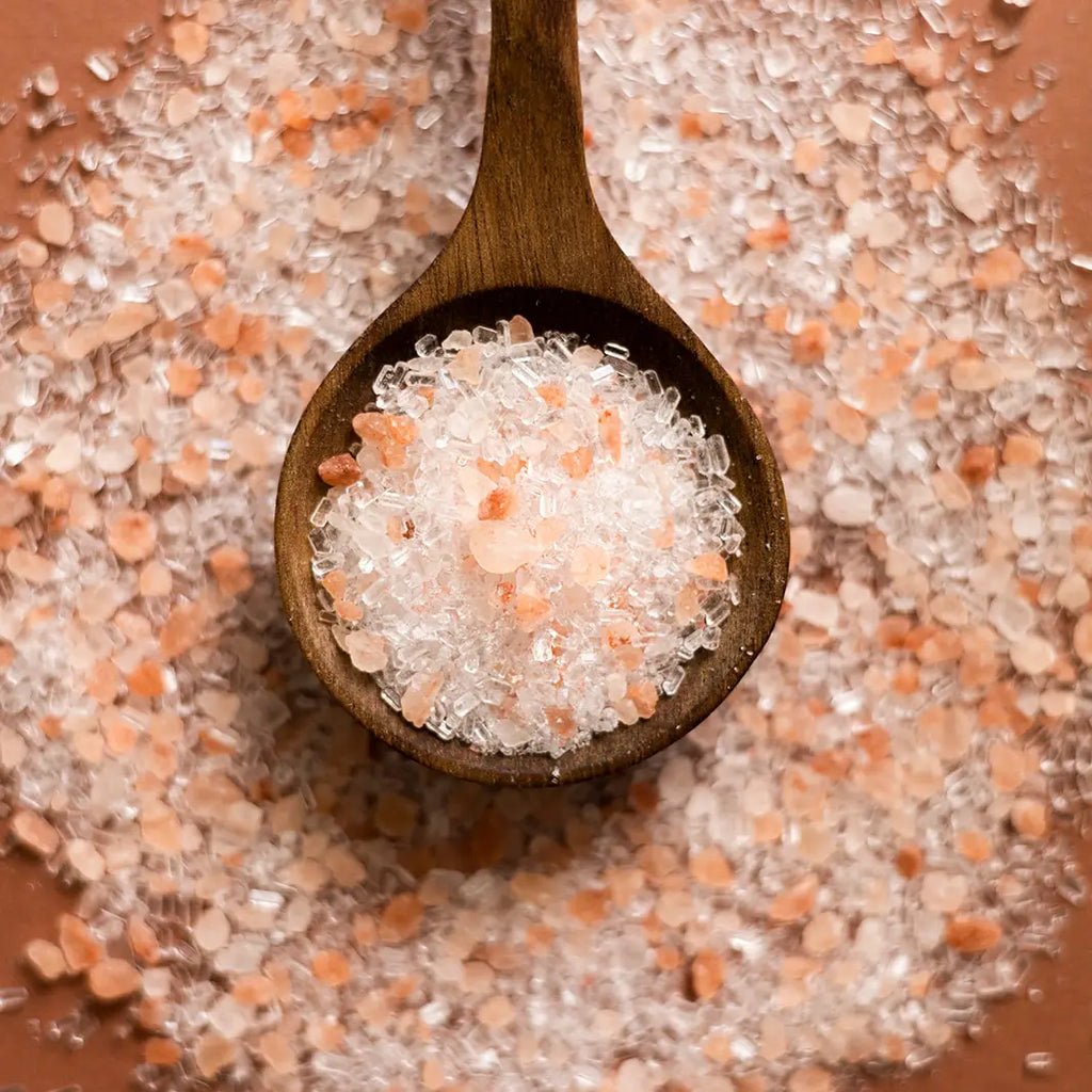 Wooden spoon filled with pink and white salt crystals on a bed of salt.