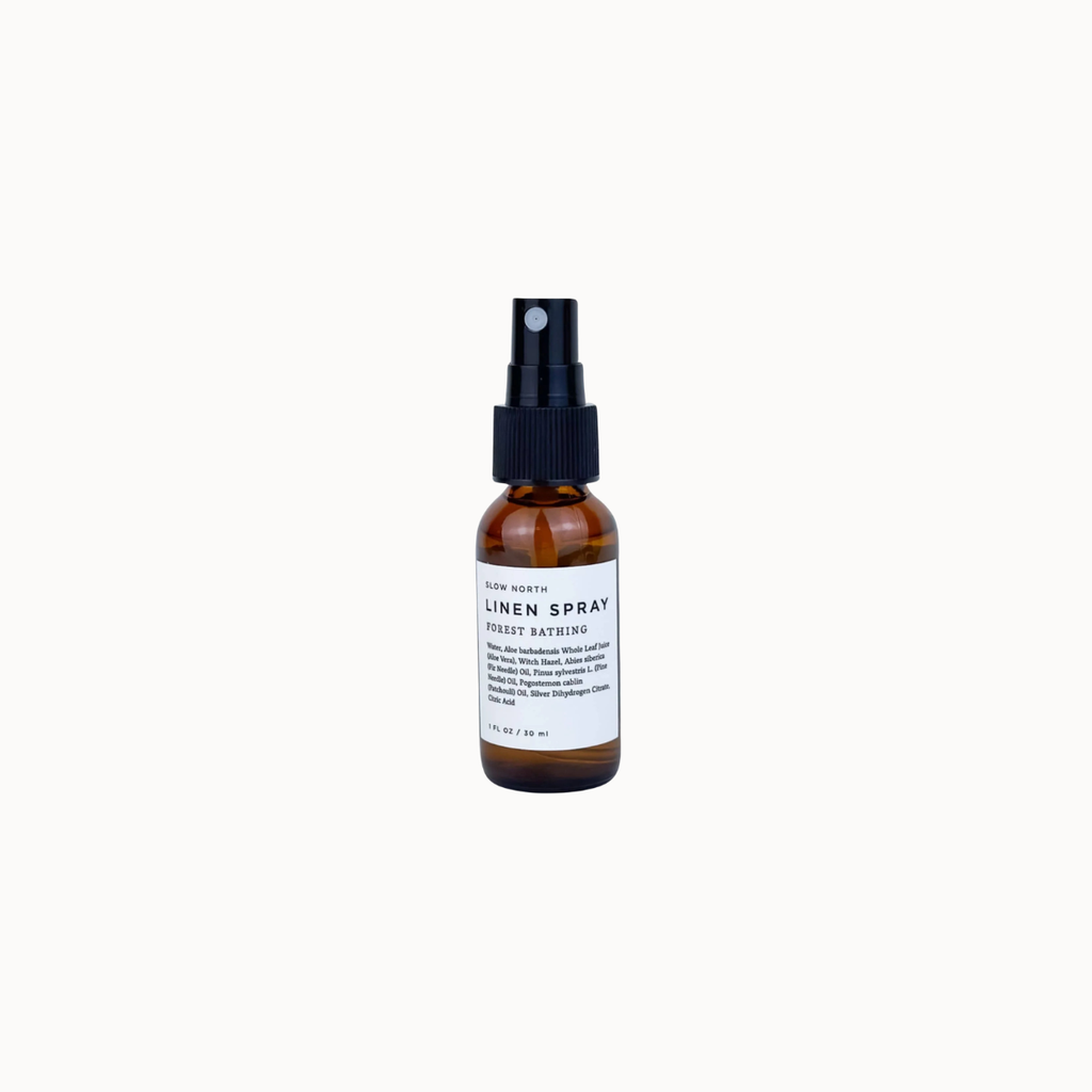 A small amber glass spray bottle with a black pump and a white label reading 'LINEN SPRAY' and 'FOREST BATHING', centered on a white background.