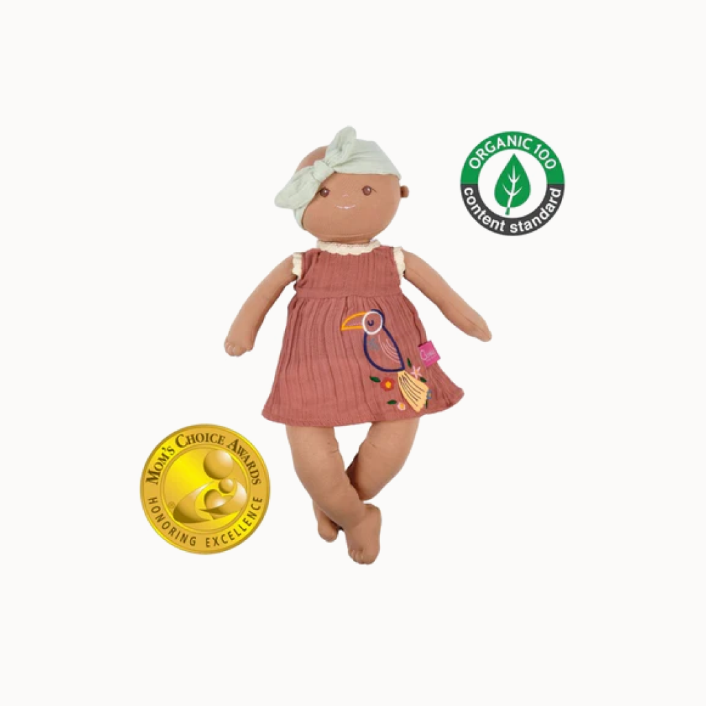 Baby doll with light green headband and brow dress that has a toucan illustration on it