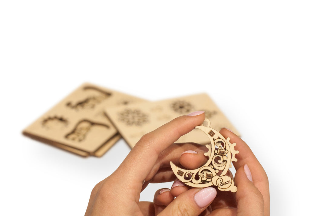 A person's hand holding a moon shaped wooden ornament 