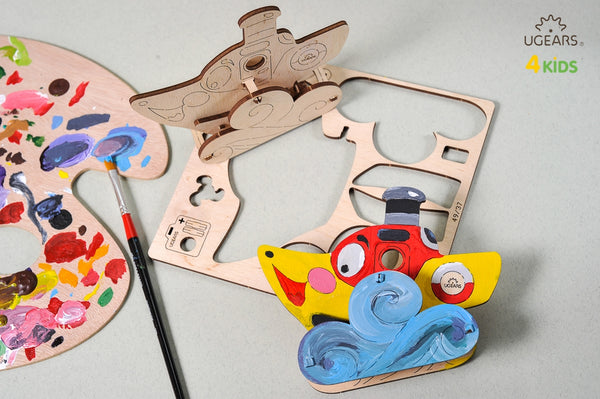Colorful toy steamboat with a red mouth and blue waves on a gray background, featuring UGears Kids branding.