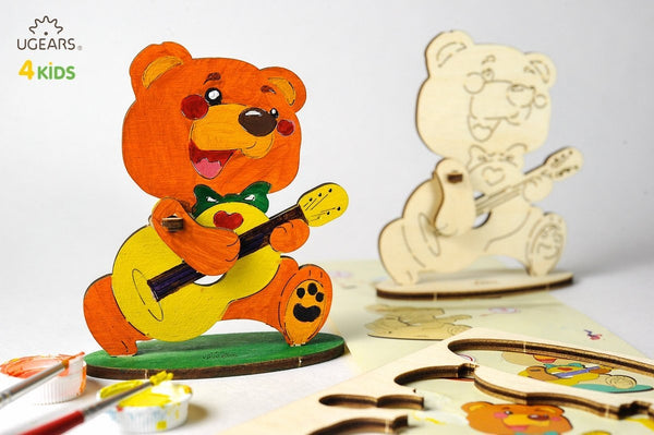 Colorful wooden toys on a table with painting supplies and UGEARS branding.