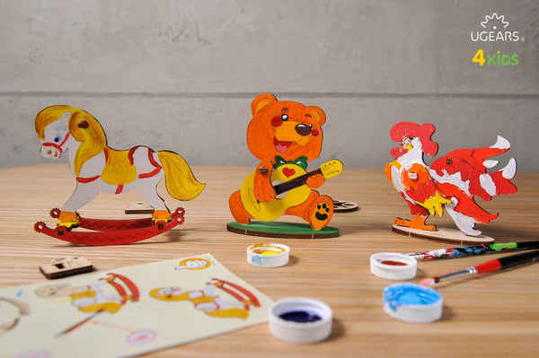 Colorful wooden toys on a table with painting supplies and UGEARS branding.
