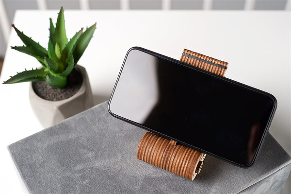 Smartphone on a wooden stand with a plant in the background