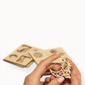 A person's hand holding a moon shaped wooden ornament 