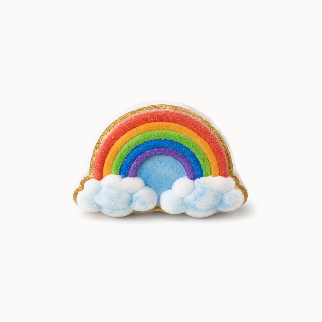 Colorful rainbow-shaped bath bomb on a white surface with a woven basket in the background.