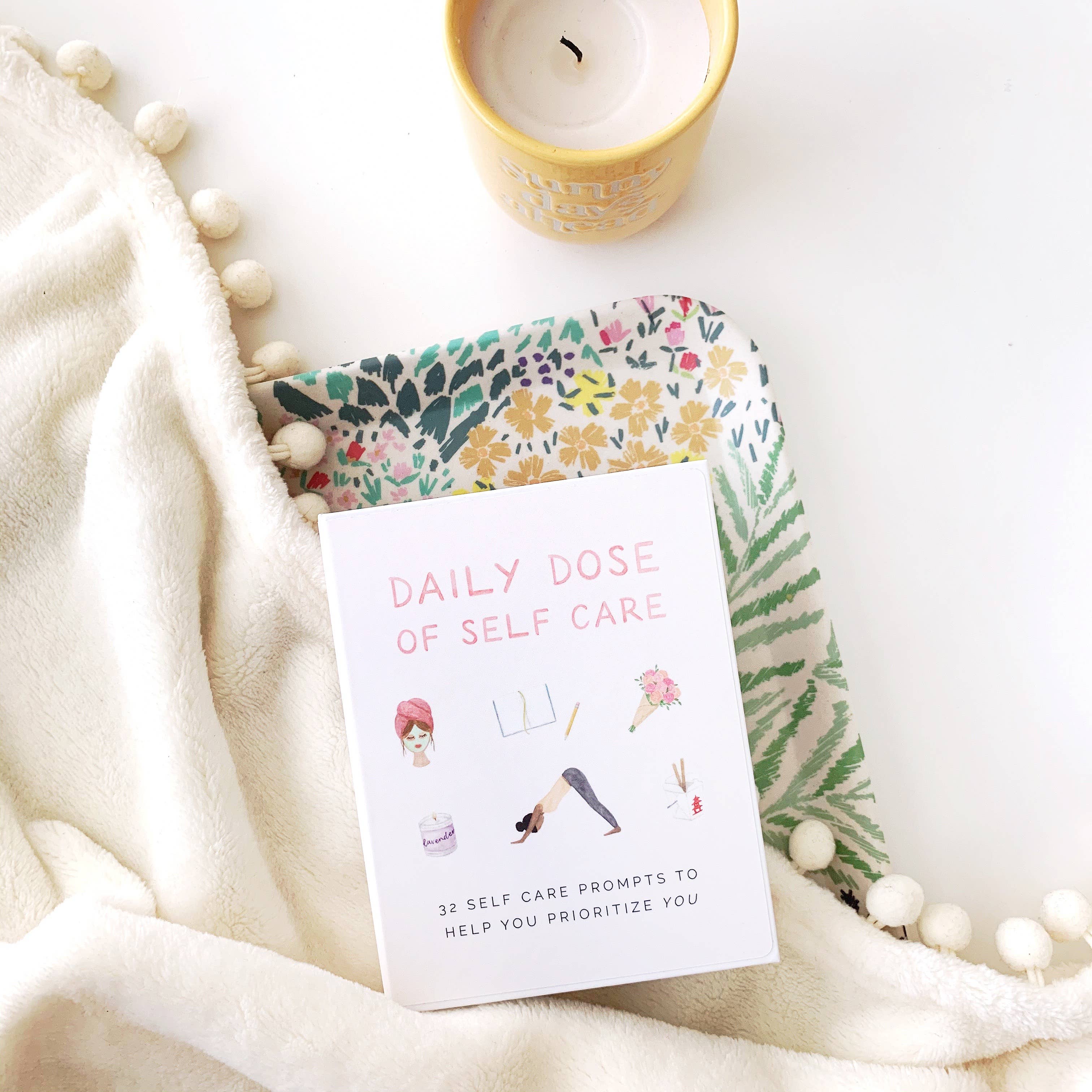 Notebook with 'Daily Dose of Self Care' on a soft surface with a candle and decorative elements.