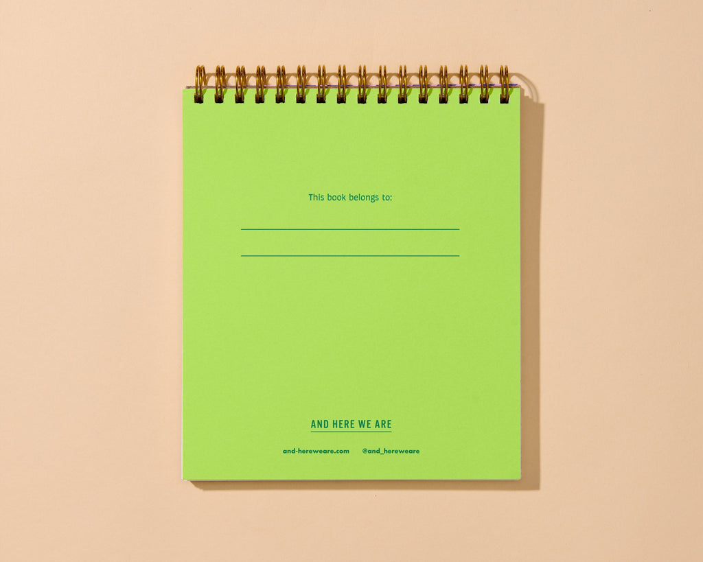 A lime green spiral-bound notebook with gold-toned metal wire binding, shown standing upright against a warm beige background. The cover has printed text including 'This book belongs to:' with blank lines and 'AND HERE WE ARE' near the bottom.