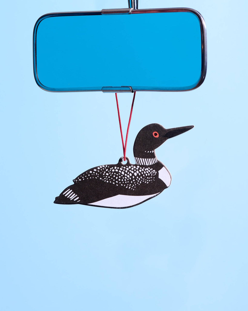 A loon-shaped car air freshener or ornament hanging from a red string beneath a blue rectangular mirror, set against a solid light blue background.