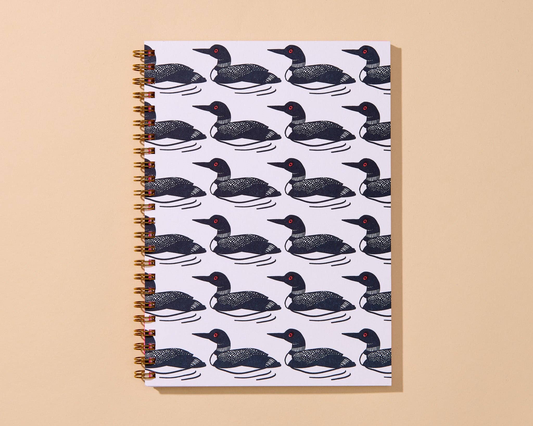 A spiral-bound notebook with a repeating pattern of black and white loons on a white cover, set against a solid beige background.