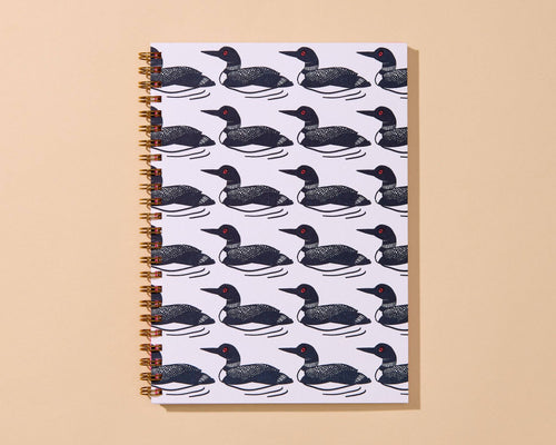 A spiral-bound notebook with a repeating pattern of black and white loons on a white cover, set against a solid beige background.
