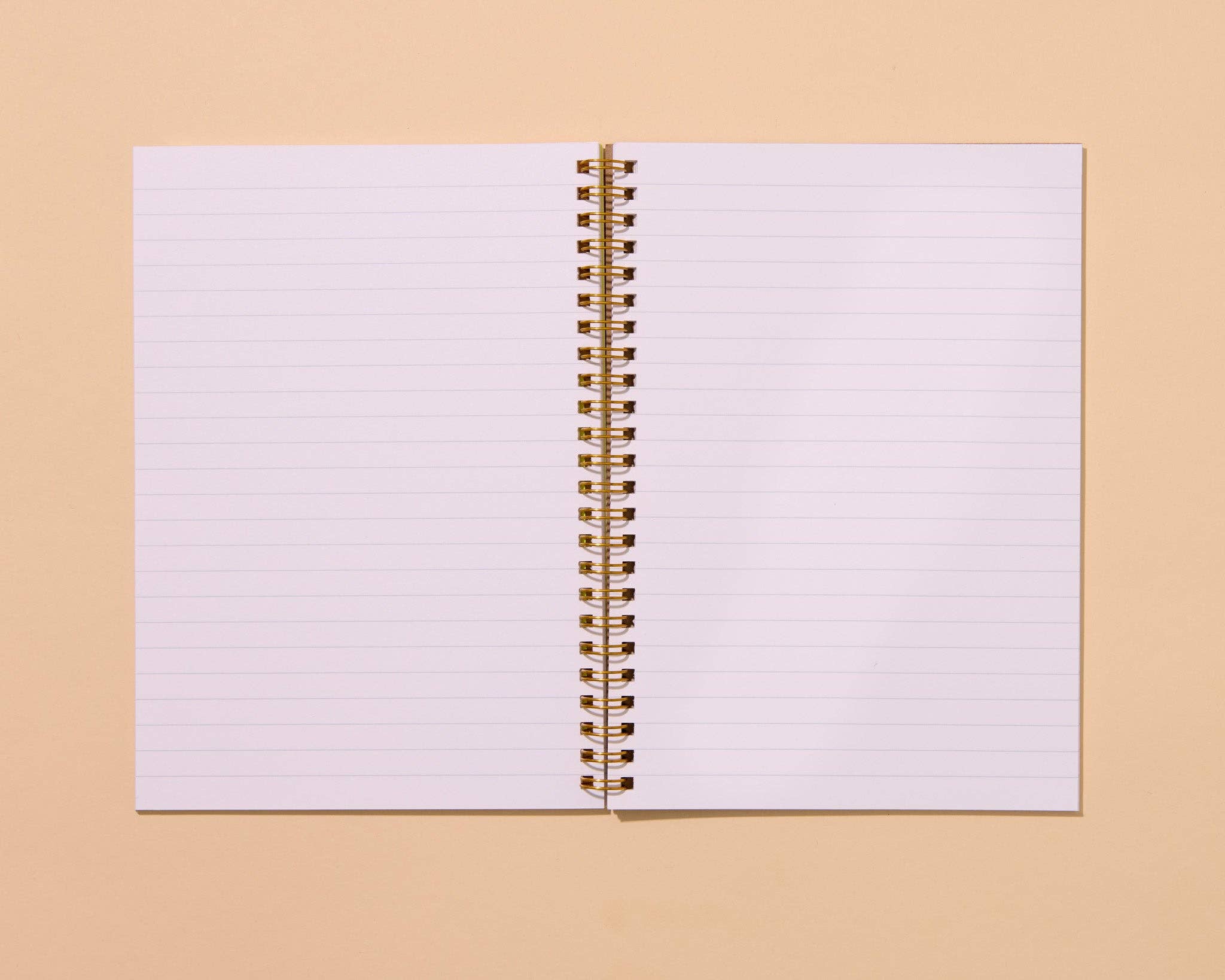 An open lined spiral notebook with gold-toned wire binding, centered on a warm beige background.