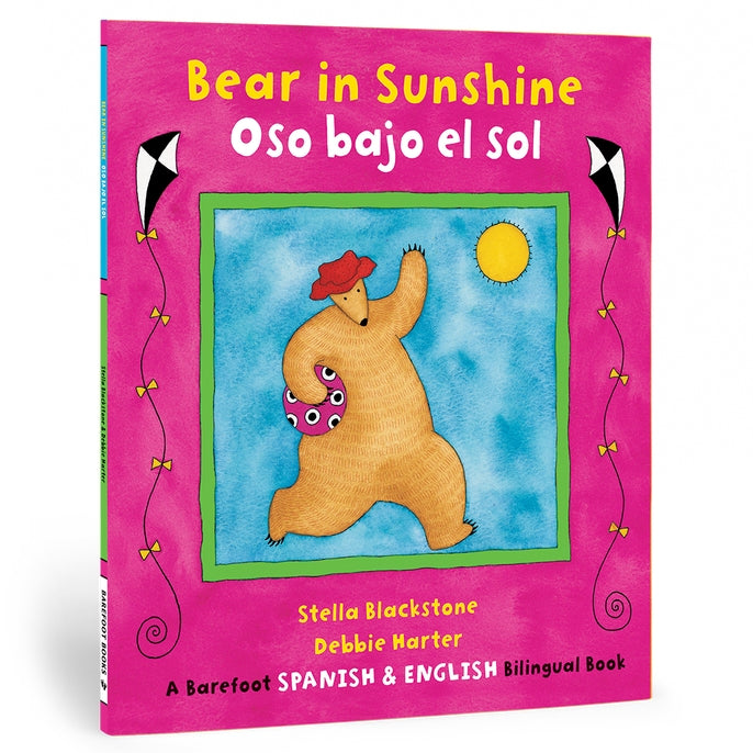 Cover of the bilingual Spanish - English book 'Bear in Sunshine' by Stella Blackstone, featuring an illustration of a cartoon bear with a sunshade in one hand and a kite in the air in the background, set against a pink background with decorative elements.