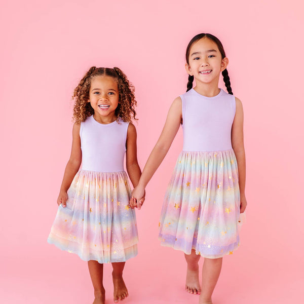 Two young girls wearing matching dresses with a colorful pattern on a pink background