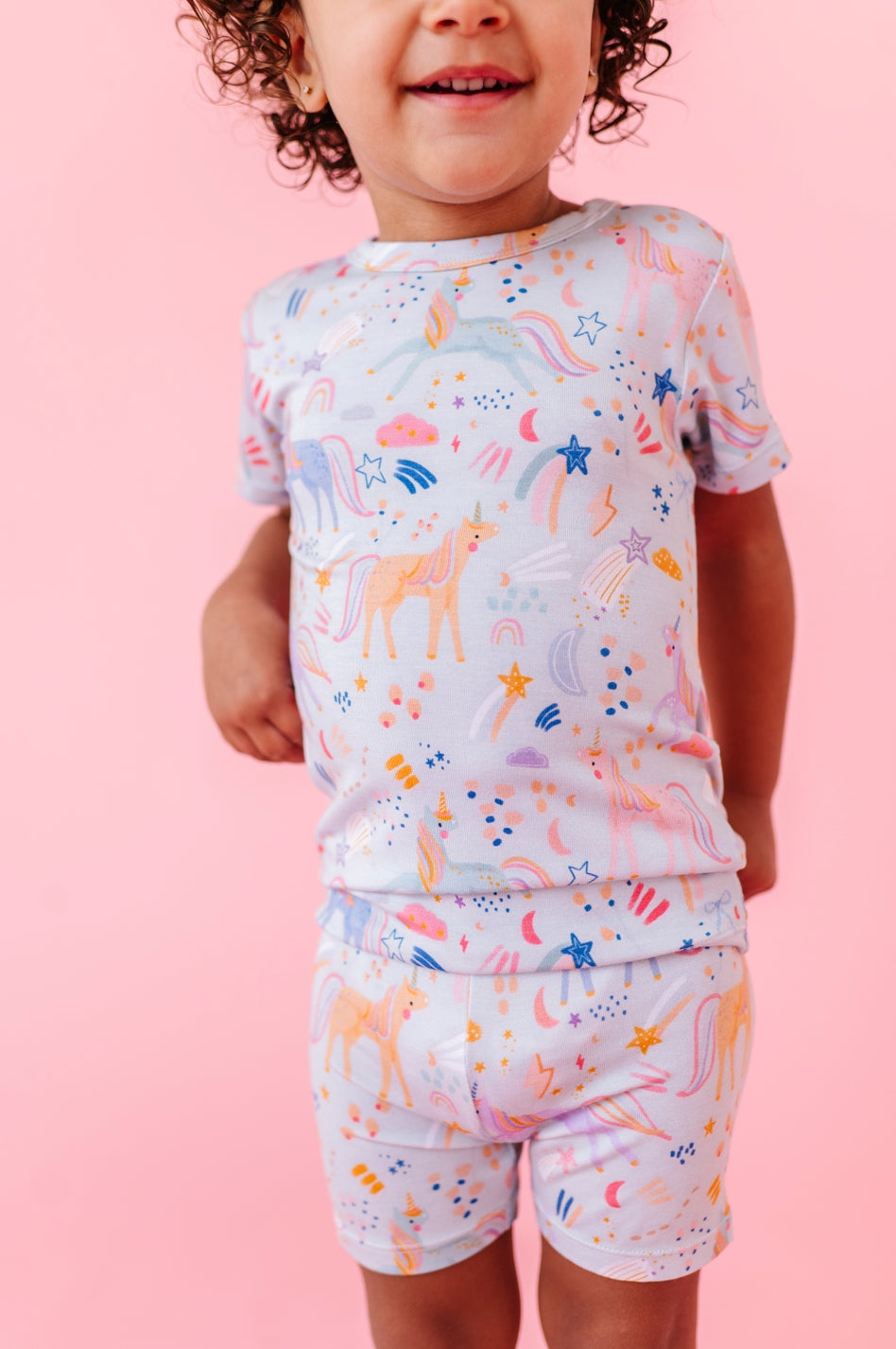 Child wearing a colorful pajama set with animal prints on a pink background
