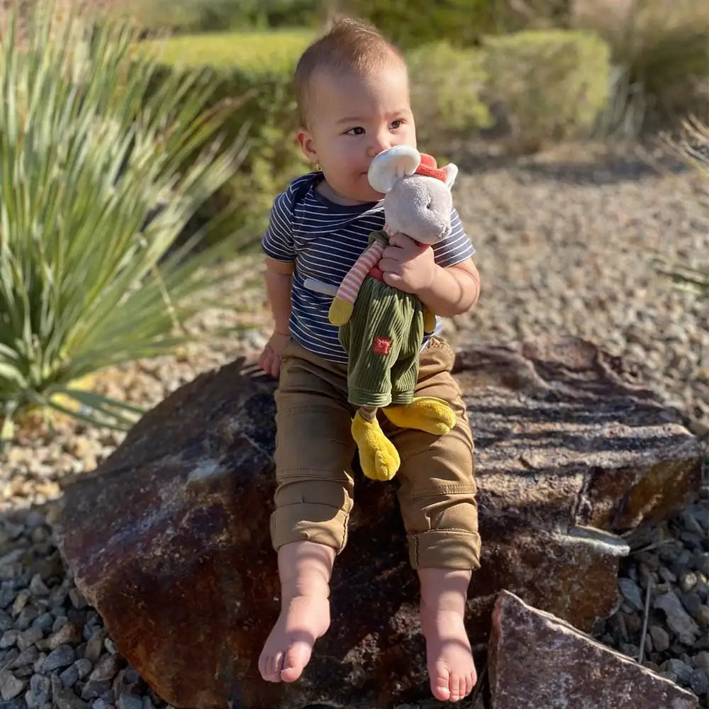 Child sitting on a rock holding a toy, surrounded by greenery