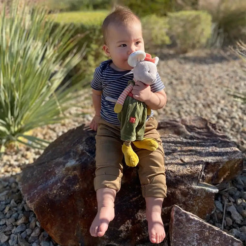 Child sitting on a rock holding a toy, surrounded by greenery