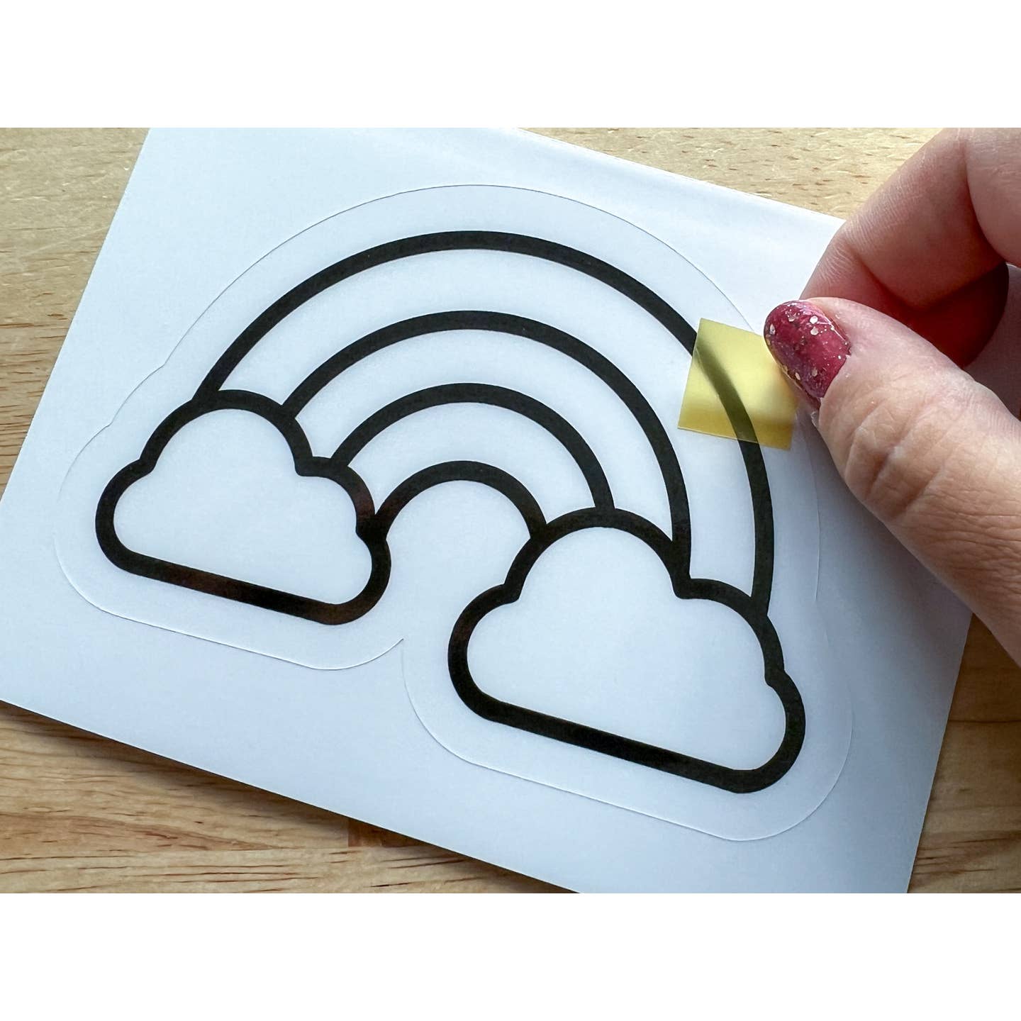 Hand applying a rainbow and cloud decal to a surface with a small yellow object.