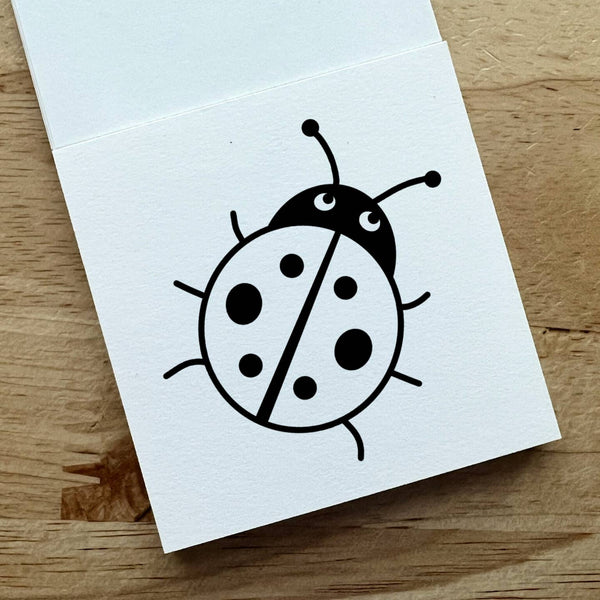 White card with a black ladybug illustration on a wooden surface