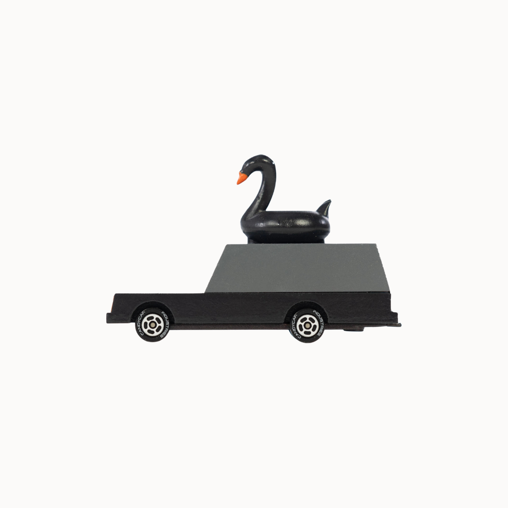A black toy car with a glossy black swan figurine sitting on its flatbed, set against a plain off-white background.