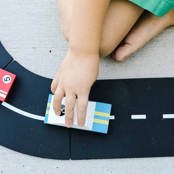 Child's hand interacting with a toy car on a black road mat.
