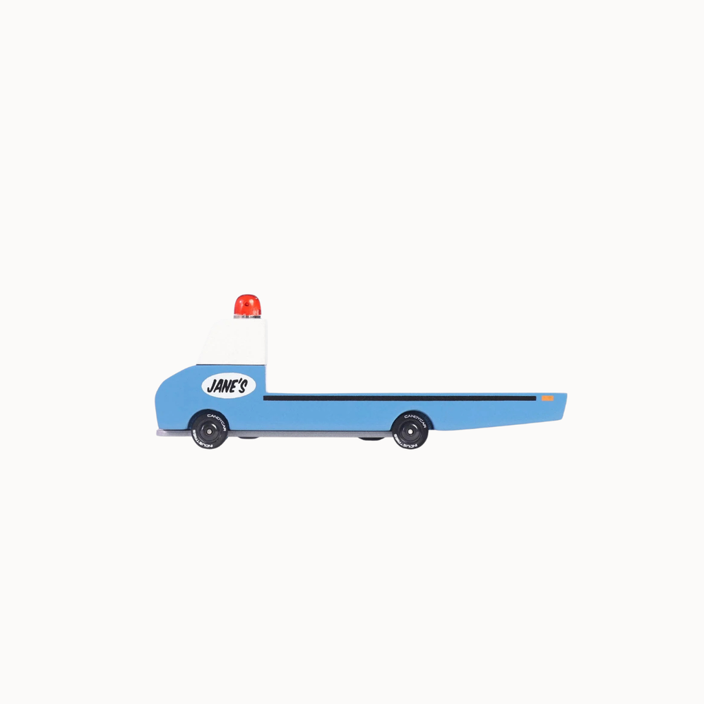A side-view toy flatbed truck, styled like a Jane's car, featuring a light blue cab, white cargo bed, black wheels, and a red siren on top, set against a solid off-white background.