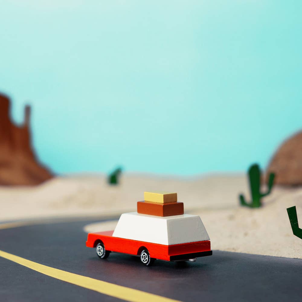 Toy car with luggage on a desert road with cacti and mountains in the background