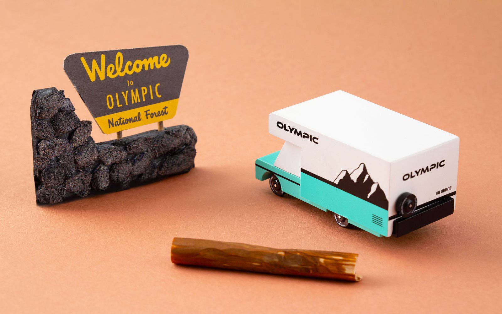 Toy van with 'Olympic' branding next to a sign and rock on a beige background