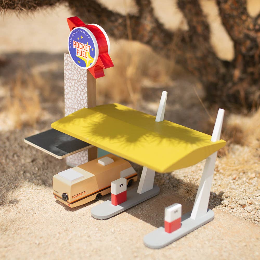 Toy fuel station with a vehicle and 'Rocket Fuel' sign on a sandy background