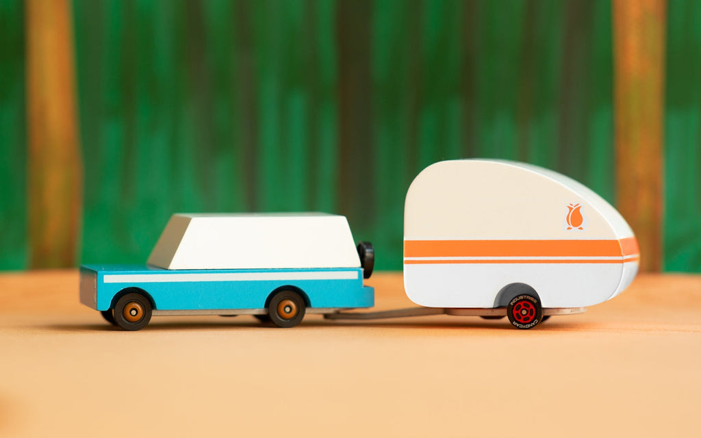 Toy van with a camper trailer on a wooden surface with a blurred green background