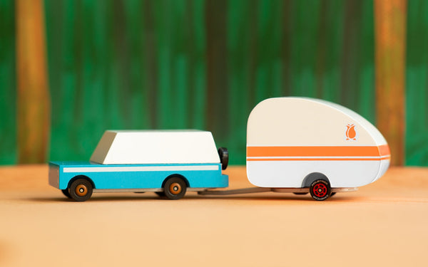 Toy van with a camper trailer on a wooden surface with a blurred green background
