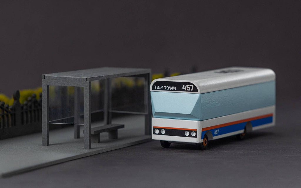 Model bus with 'Tiny Town' branding next to a bus stop on a dark background