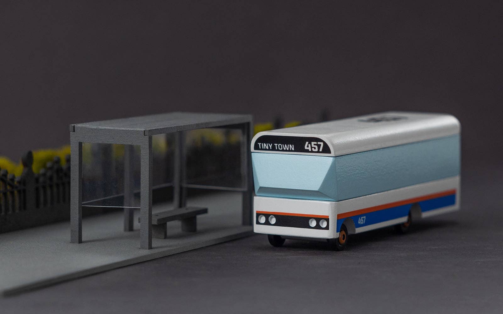 Model bus with 'Tiny Town' branding next to a bus stop on a dark background