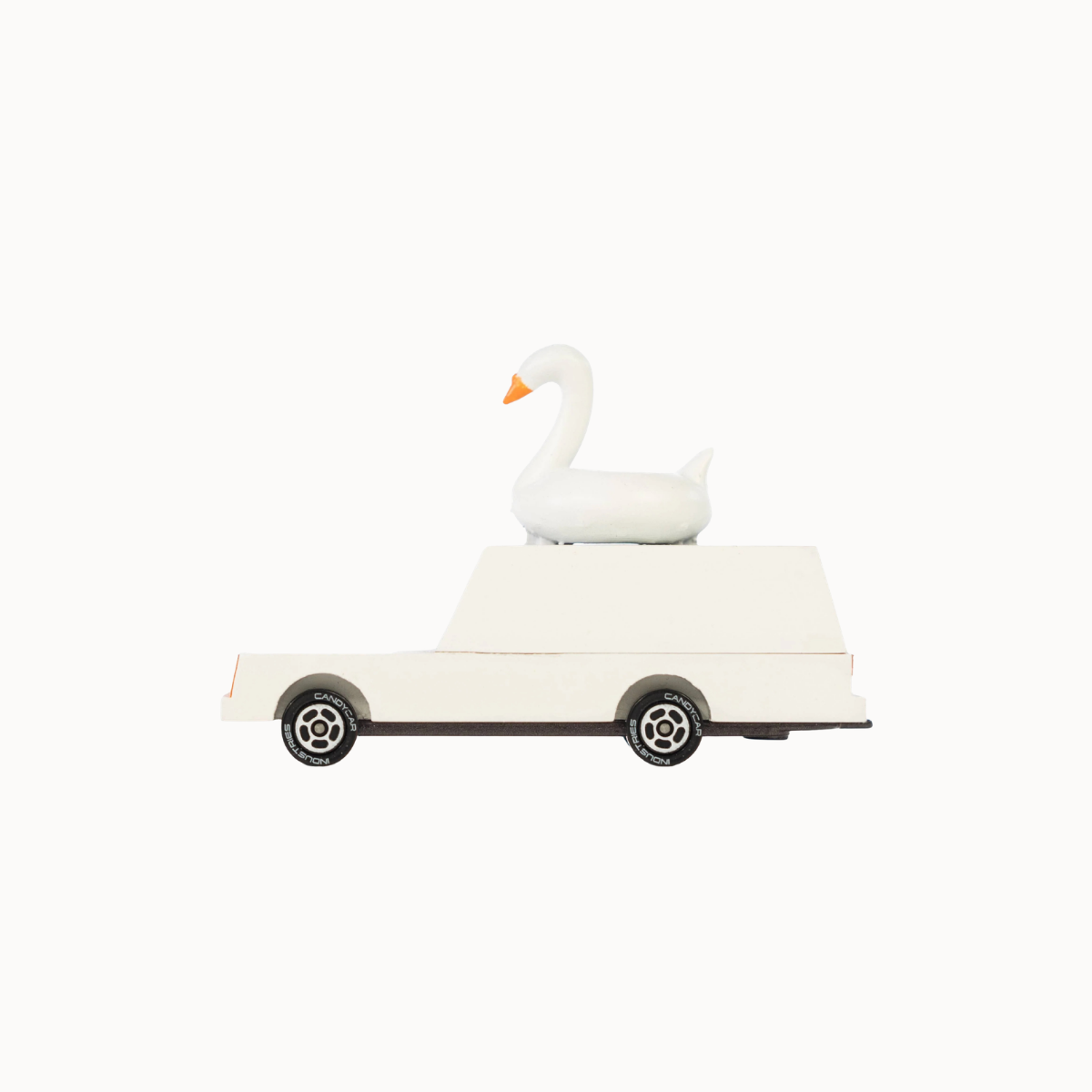 A white swan figurine with an orange beak sitting on top of a white toy car with black wheels, isolated on a solid off-white background.
